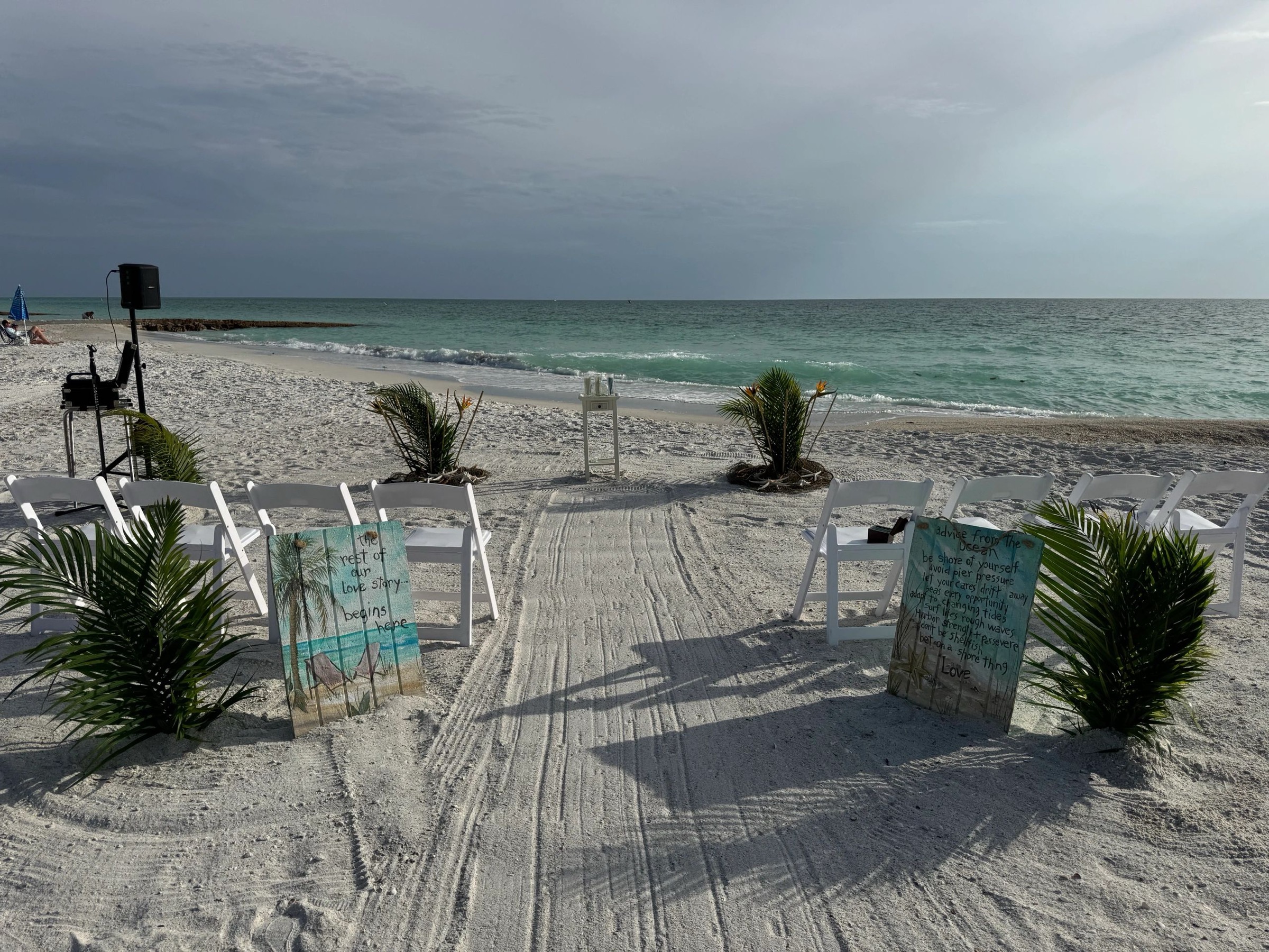 Combed sand aisle lined with palms, white chairs and painted signs by the Gulf, Beach Breeze Weddings