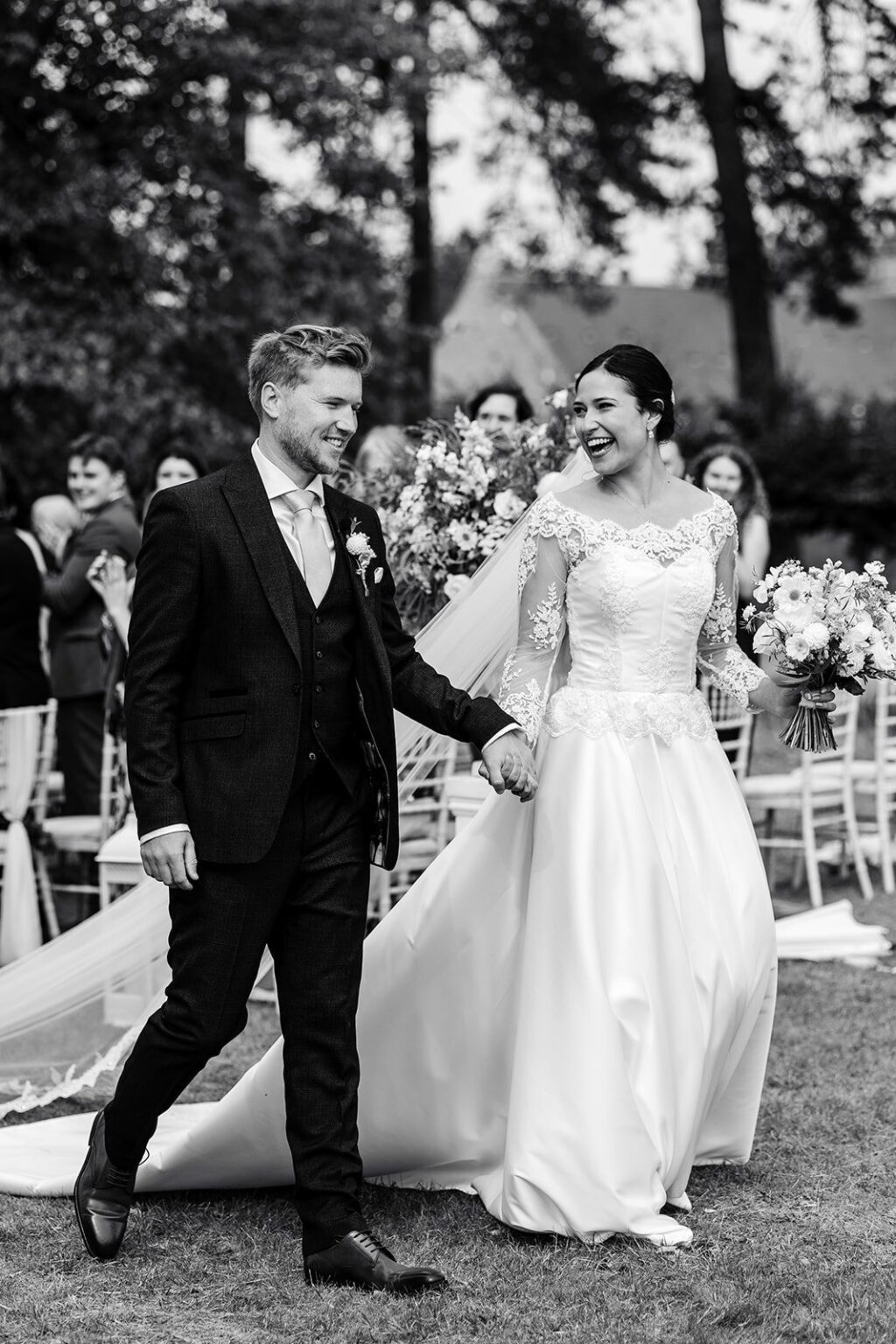 A laughing couple in black and white, the bride in a lace-sleeved gown with a long train, Beatrice Espinosa Bridal