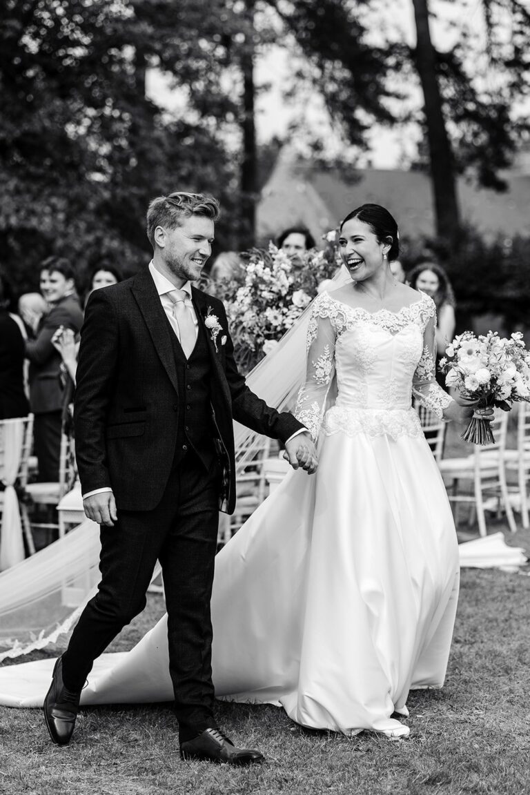 A laughing couple in black and white, the bride in a lace-sleeved gown with a long train, Beatrice Espinosa Bridal