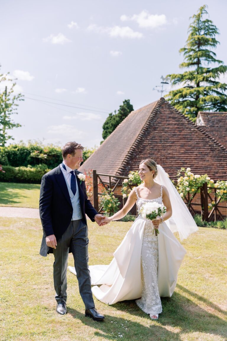 A couple holding hands, the bride in a fitted lace gown with a detachable satin overskirt, Beatrice Espinosa Bridal