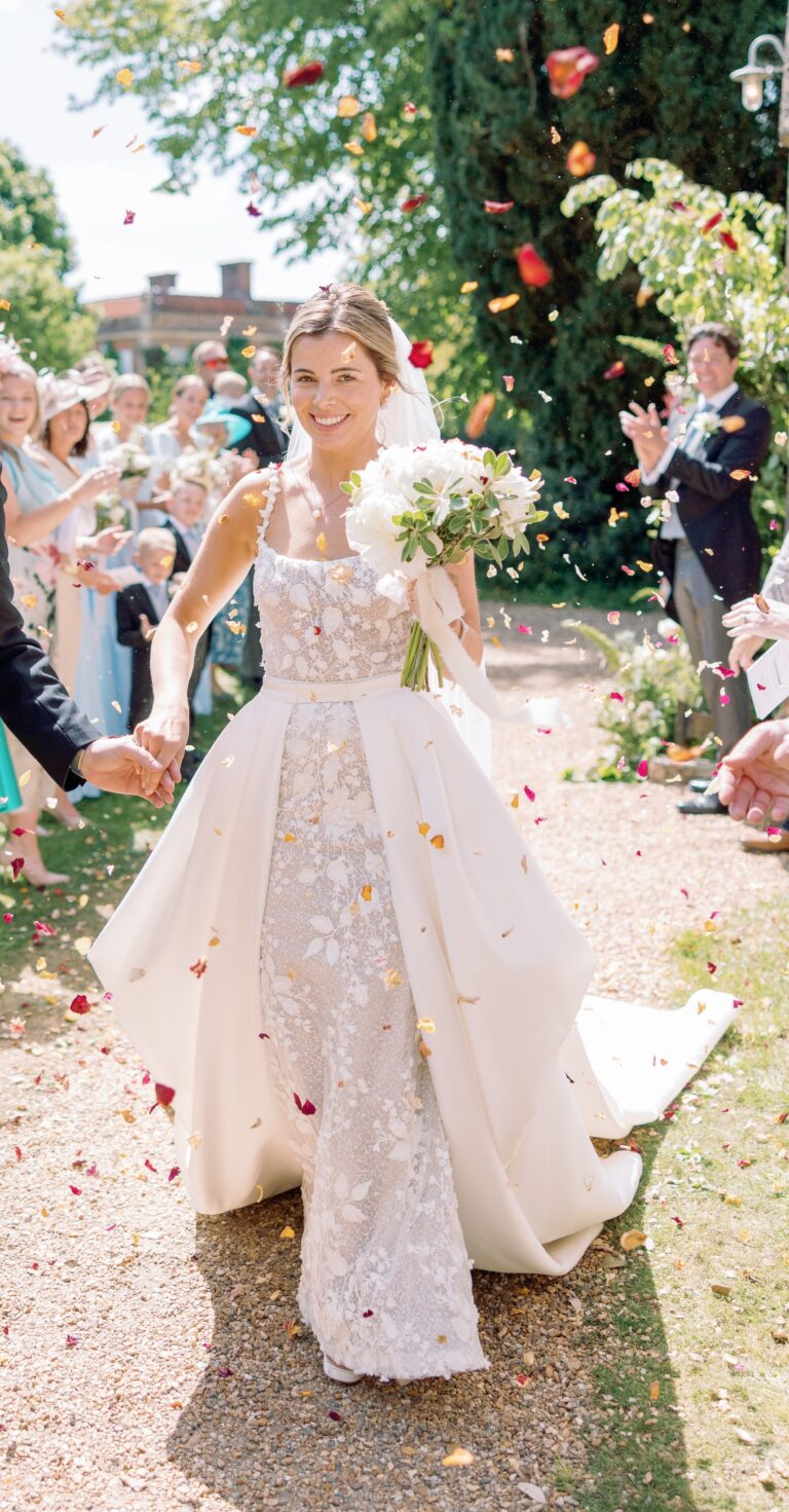 A bride in an embroidered gown with a detachable overskirt walking through petals and confetti, Beatrice Espinosa Bridal