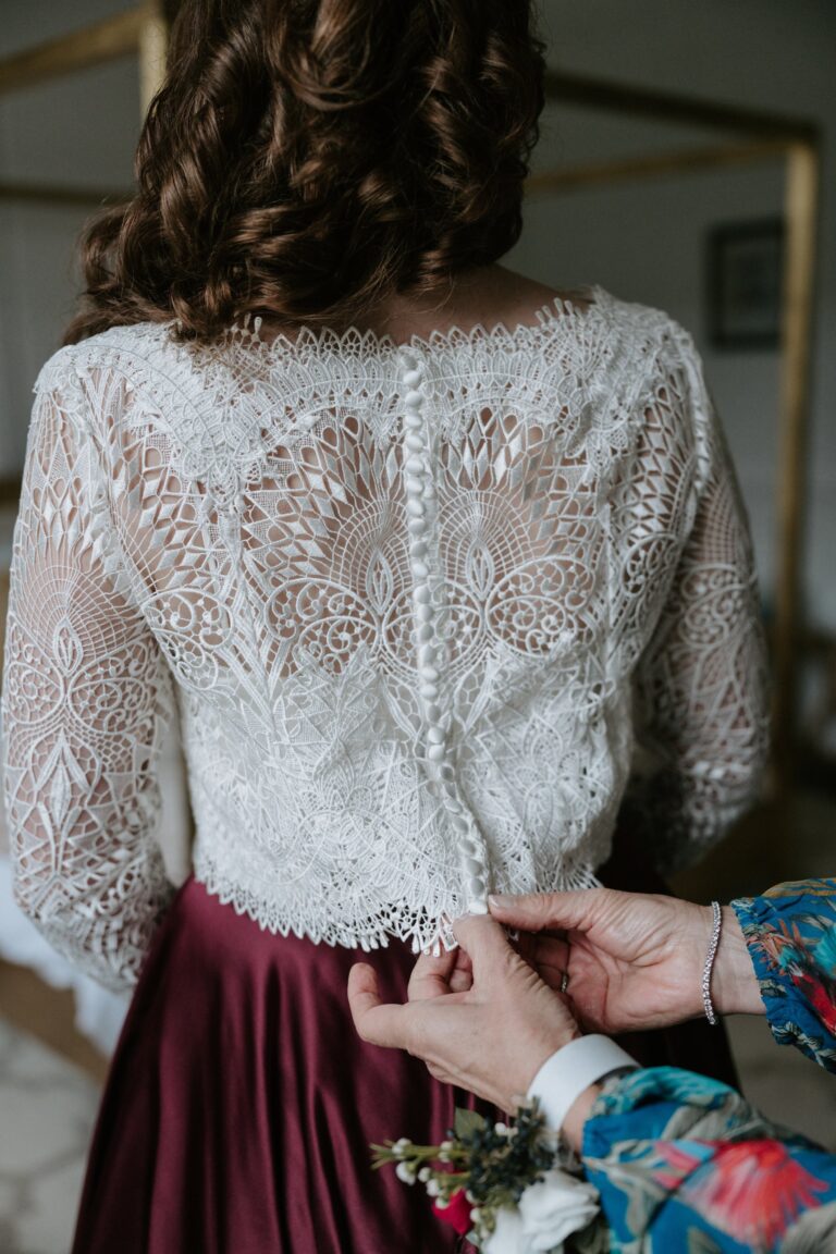 A bride having the covered buttons on the back of her lace bridal top fastened, Beatrice Espinosa Bridal