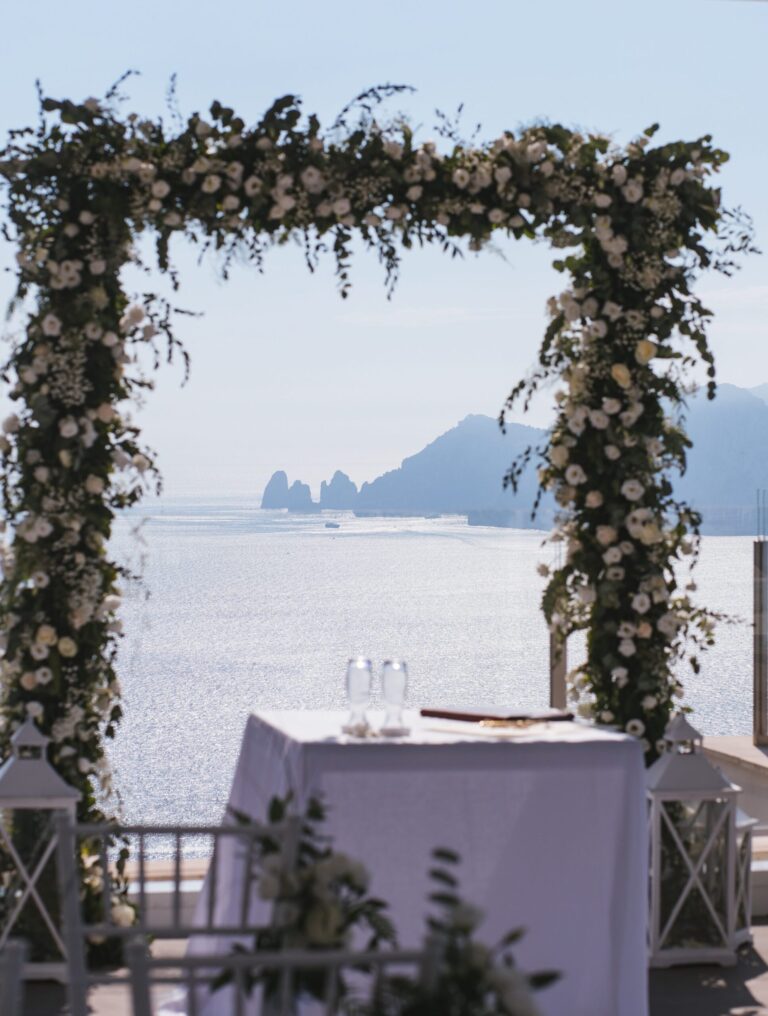 A floral arch frames the Faraglioni of Capri across open water, Bella Sposa