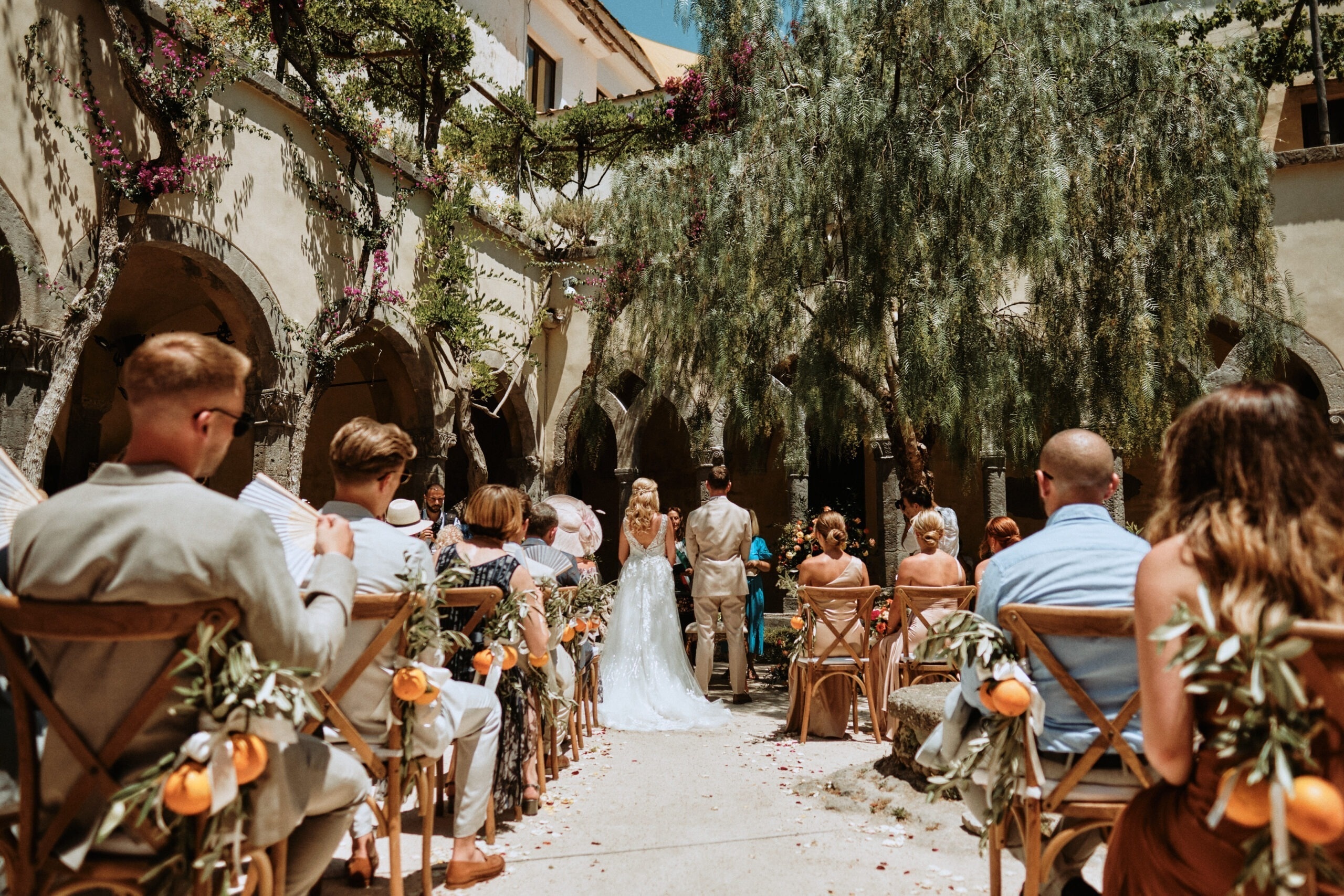 Ceremony chairs dressed with whole oranges and olive branches, under a vaulted arcade, Bella Sposa