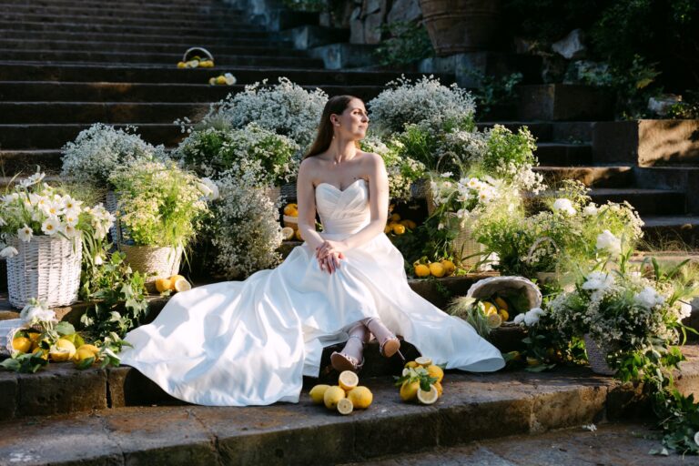 The bride alone on stone steps banked with baskets of lemons, Bella Sposa