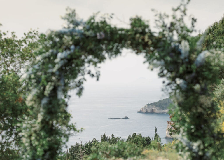 A floral arch framing the sea at a Paxos olive grove wedding, Belli Momenti