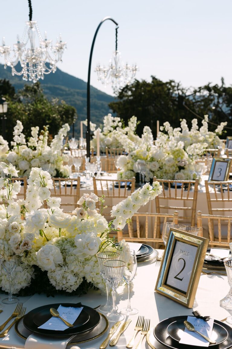 A white floral centrepiece beneath chandeliers at a Corfu wedding, Belli Momenti