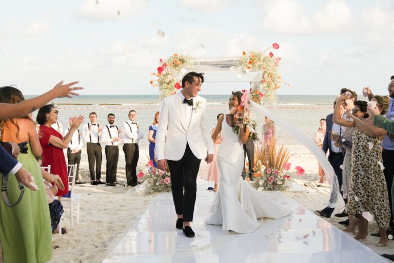 Couple walking back down a white aisle after a beach ceremony under a floral arch, Better Together Mexico