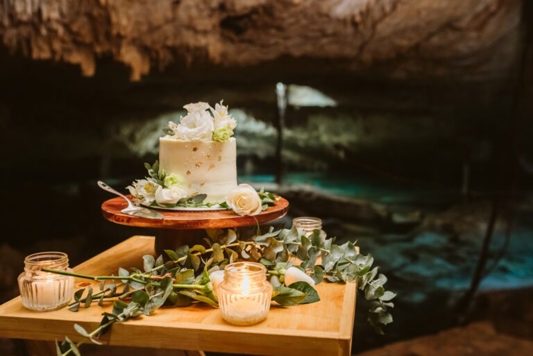 A wedding cake with white flowers set on a table in a cenote, Better Together Mexico