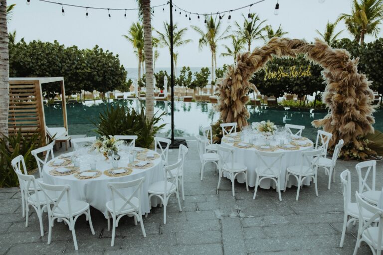 Round tables beside a pool with a pampas grass arch behind, Better Together Mexico