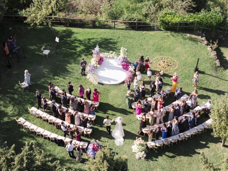From the air: a circular ceremony, guests in bright colours ringing it, Bianco Bouquet Weddings and Events