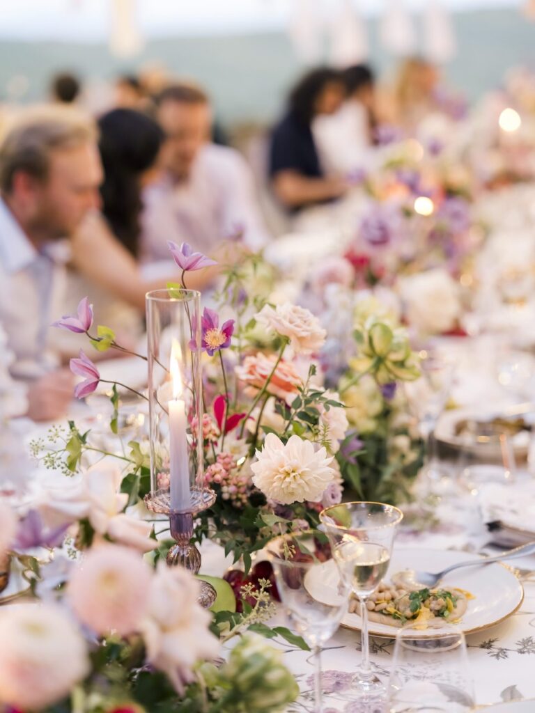 Guests at a long table dressed with dahlias, clematis and roses, Bianco Bouquet Weddings and Events