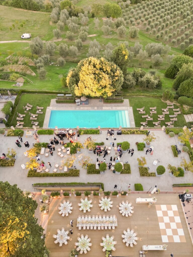 From the air: the pool terrace set for the wedding, guests at tables, olive groves beyond, Bianco Bouquet Weddings and Events