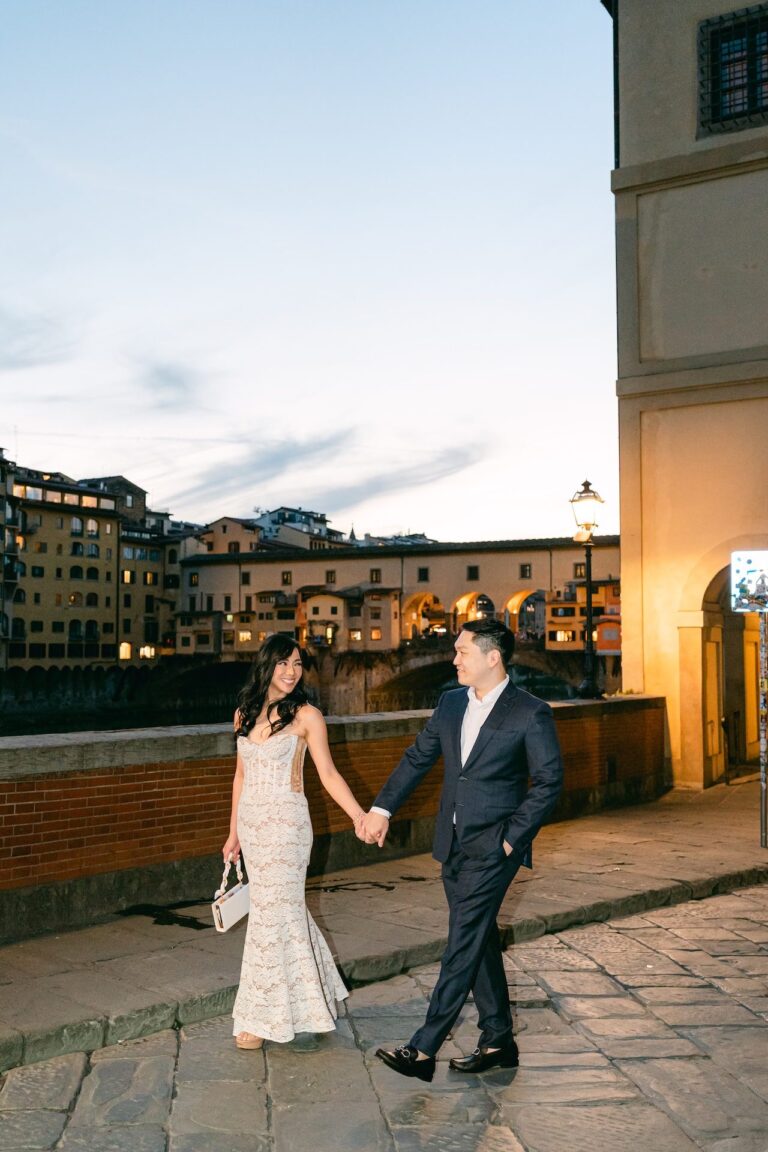 The couple hand in hand at dusk, the Ponte Vecchio lit behind them, Bianco Bouquet Weddings and Events