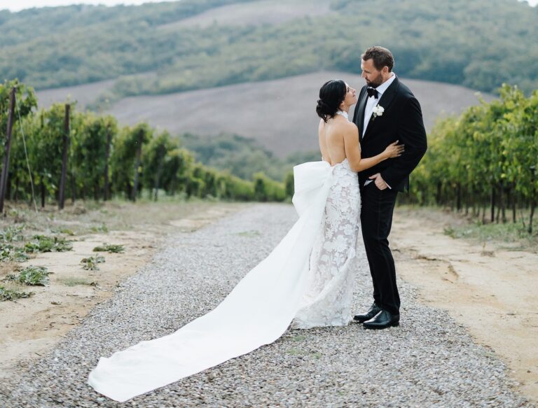 The couple on a gravel track between vines, the train spread out, Chianti hills beyond, Bianco Bouquet Weddings and Events