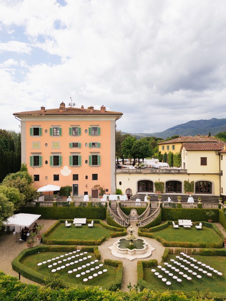 A pink villa above its box parterre, chairs set out in the garden, Bianco Bouquet Weddings and Events