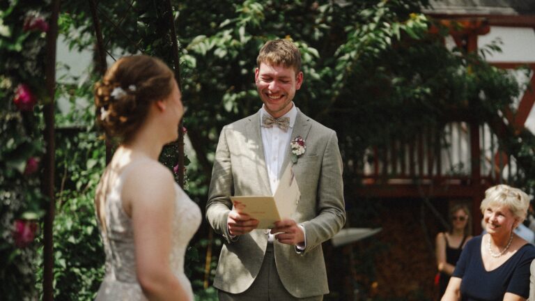 Couple laughing during their vows under a garden rose arch, Bilingual Celebrant in Europe