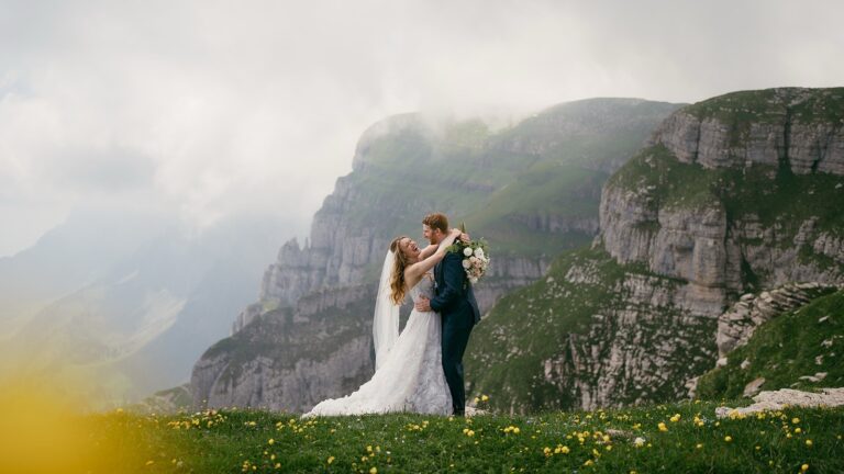 Couple embracing on a flowering alpine meadow below limestone cliffs, Bilingual Celebrant in Europe