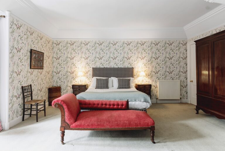 A bedroom at Forest Lodge with a red chaise at the foot of the bed, Blair Castle