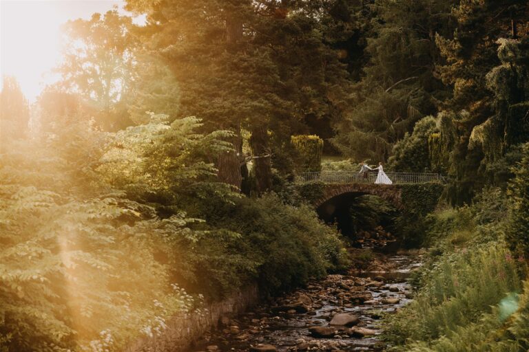 A couple on a stone bridge over the Banvie Burn in Diana's Grove, in evening light, Blair Castle