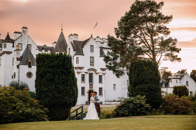 The castle at sunset with a couple on the lawn below and pines framing the view, Blair Castle