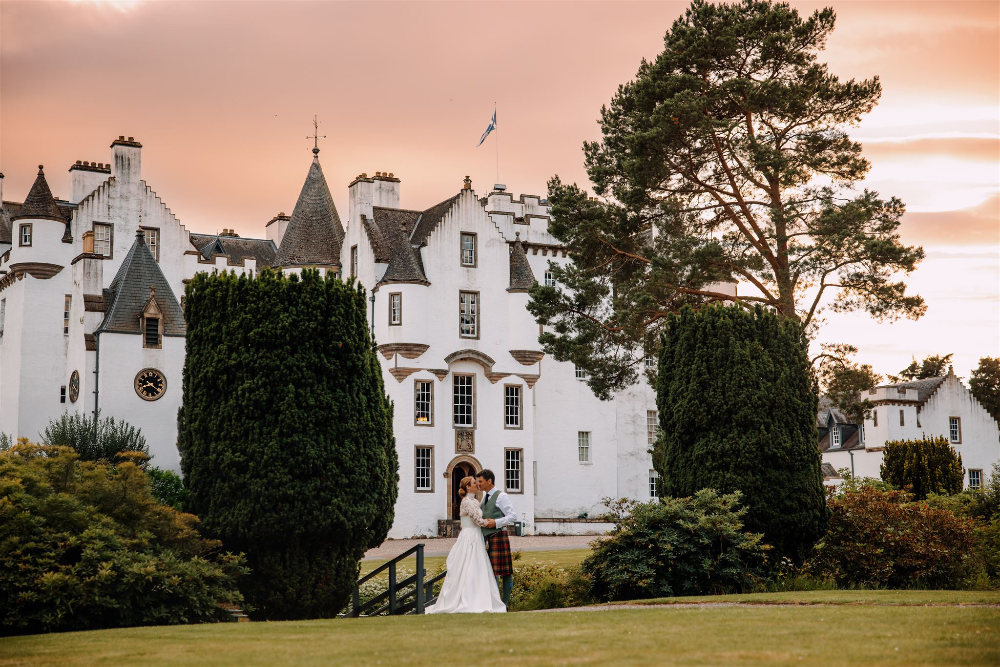 The castle at sunset with a couple on the lawn below and pines framing the view, Blair Castle