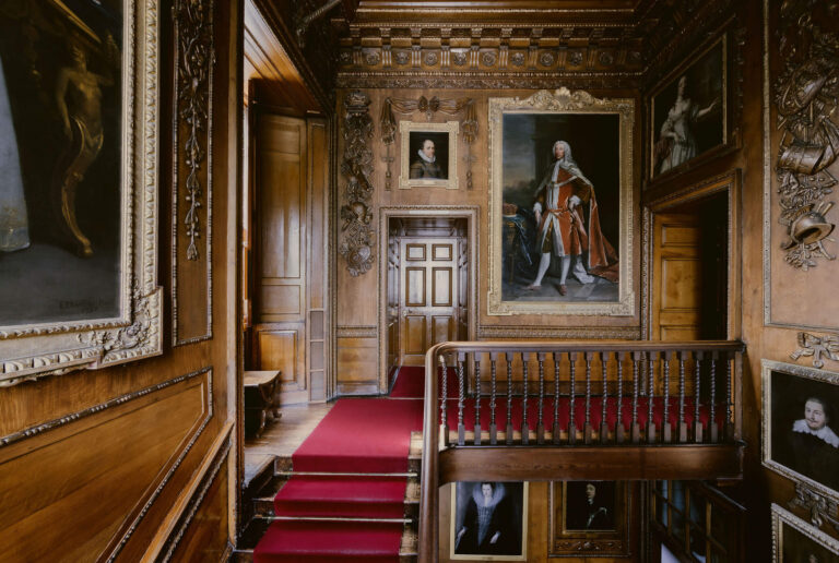 A panelled stair landing with a red carpet and family portraits, Blair Castle