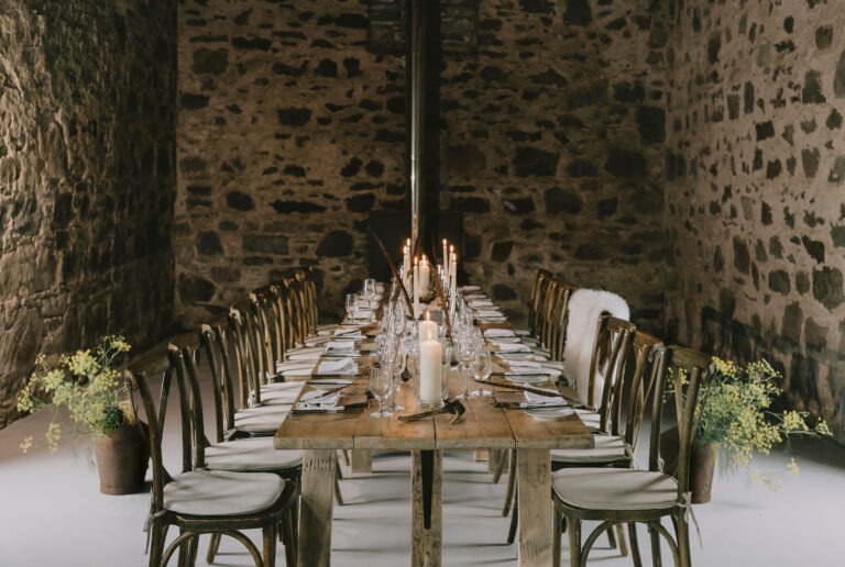 A long table with candles and wooden chairs inside the stone Clachan Barn, Blair Castle