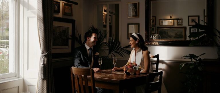 Hannah and Jonathan with champagne by the window at Hampton Manor, Solihull (frame from their teaser), Blue Ridge Films