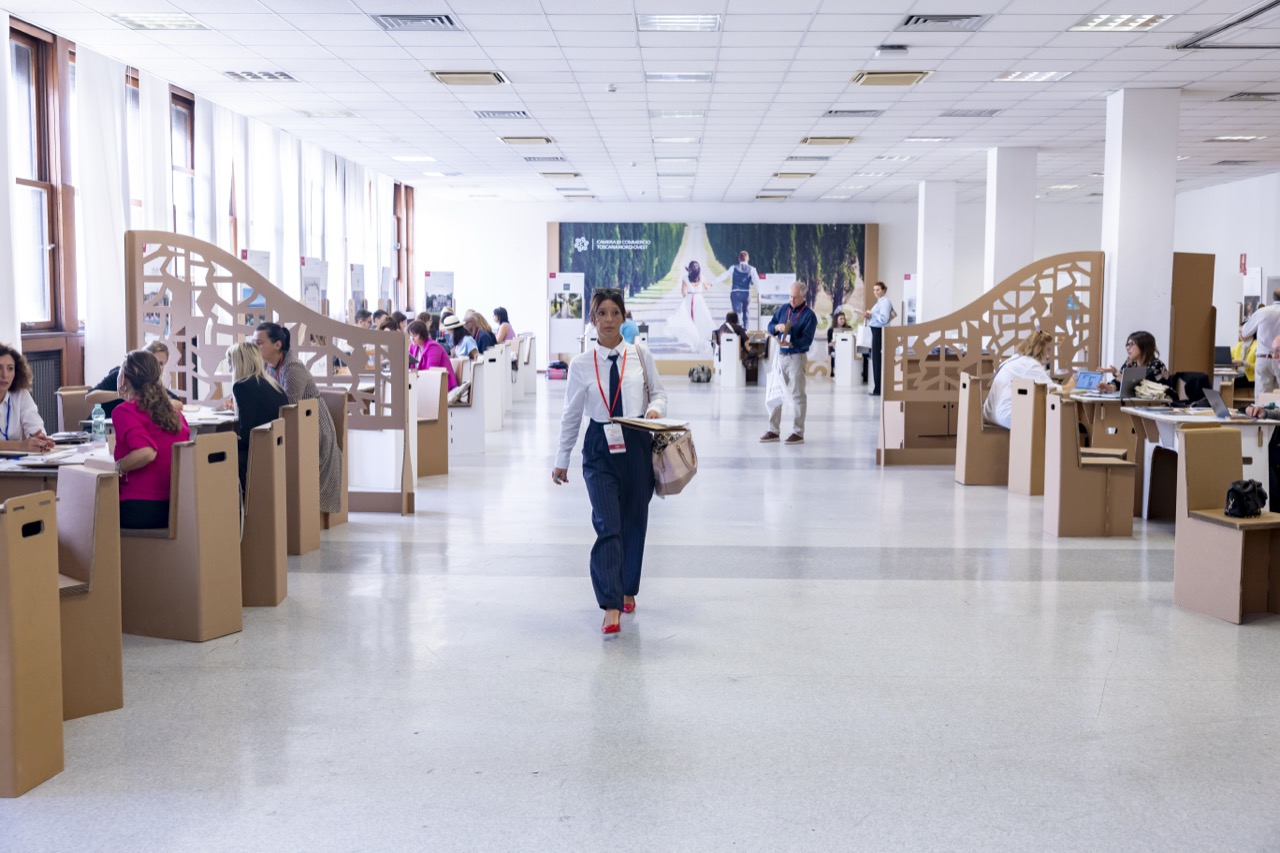 A long hall with rows of cardboard tables and display stands, with participants at their meetings