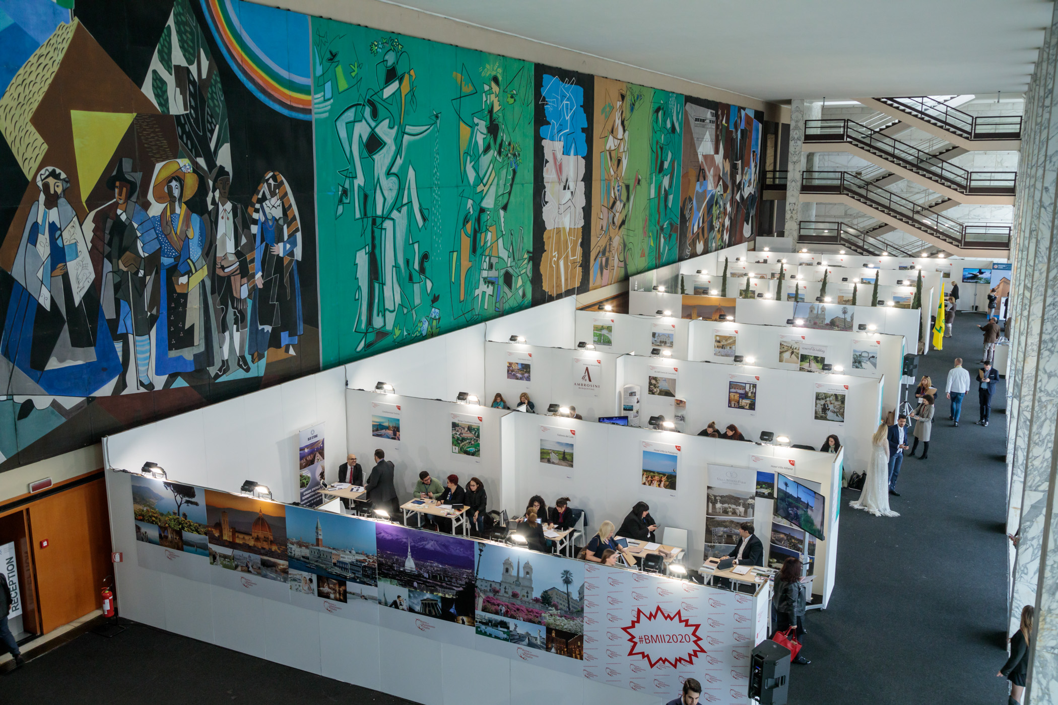 A view from above of the meeting floor, with rows of white stands and tables beside a wall of murals