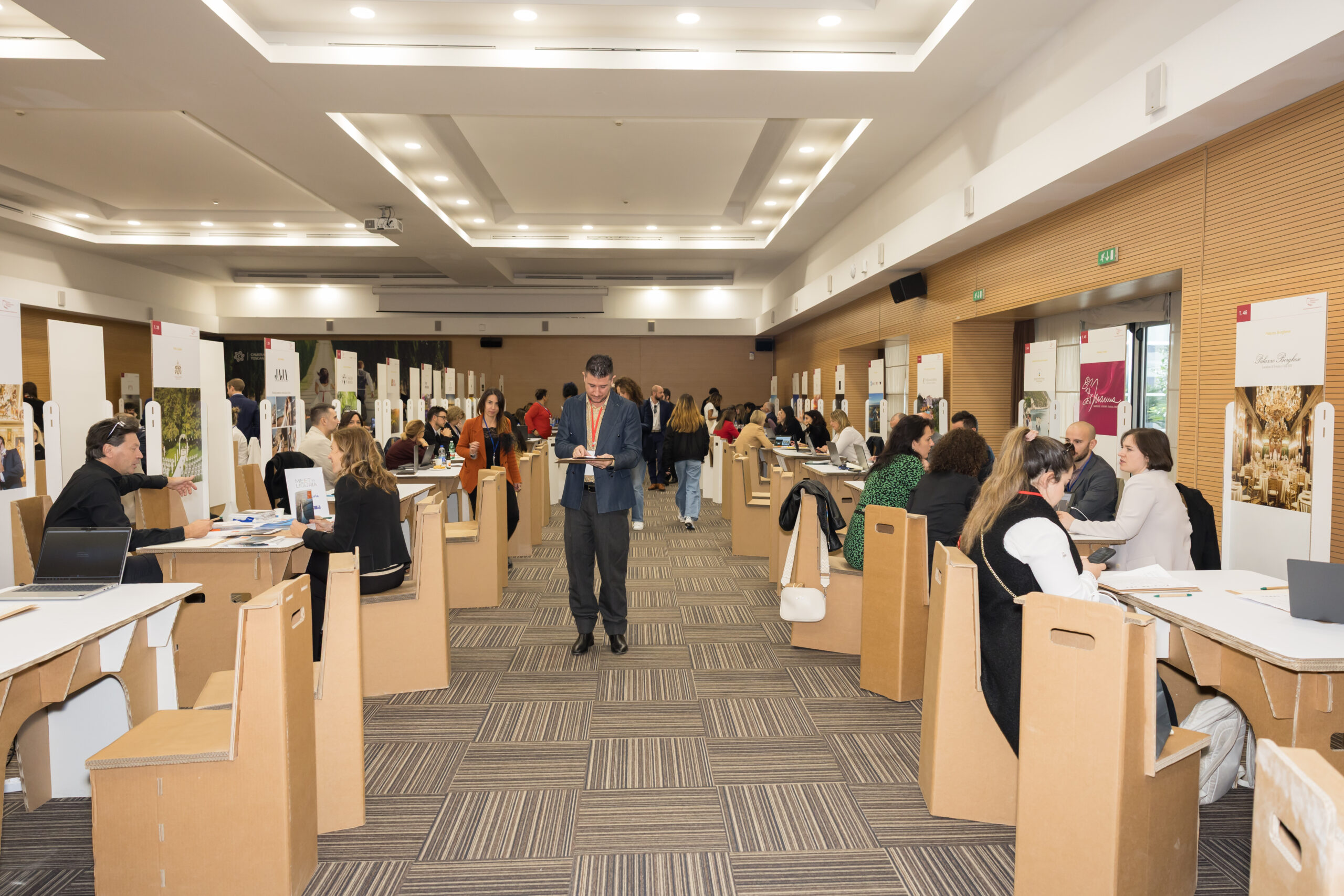 A carpeted room with wood-panelled walls and rows of tables where participants sit in meetings