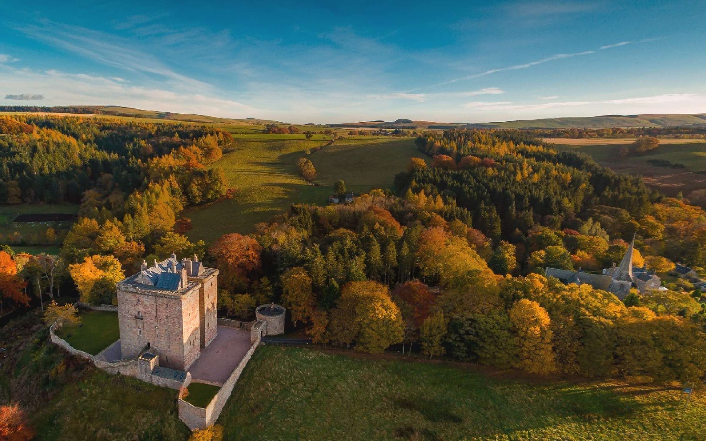 The castle and gatehouse from above in autumn, with the wooded valley and Midlothian farmland stretching beyond, Borthwick Castle