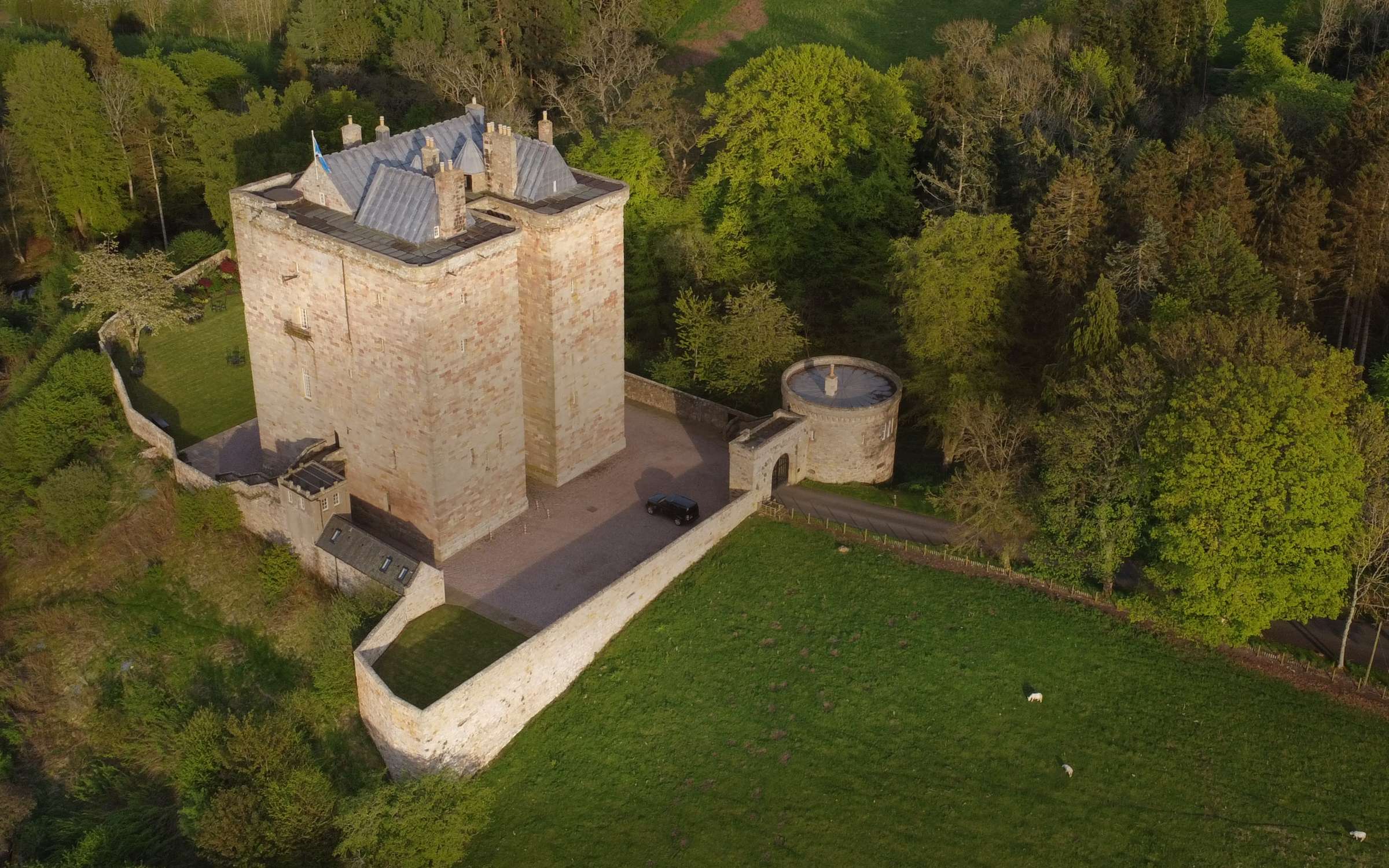 Aerial view in summer of the keep, the walled lawn and the round gatehouse tower set among trees, Borthwick Castle