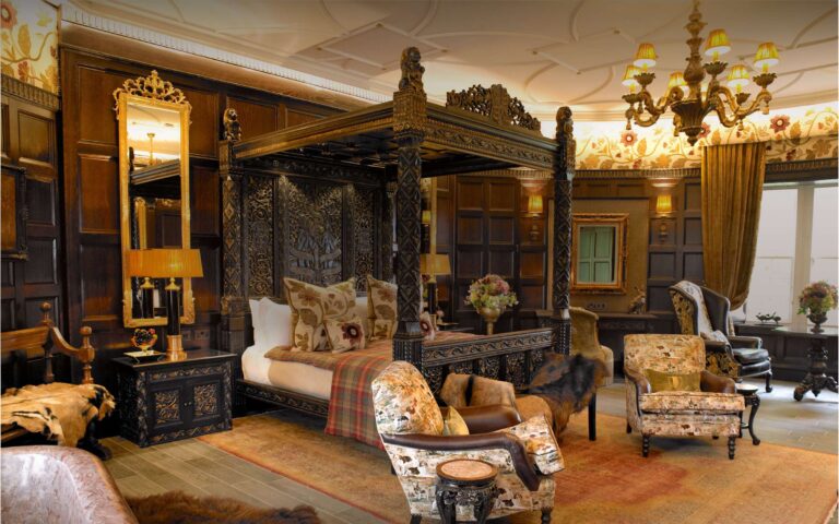 The Gatehouse suite, with its carved four-poster bed, panelled walls, chandelier and armchairs on a tartan rug, Borthwick Castle