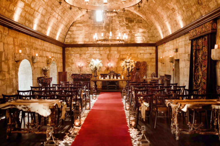 Rows of chairs with sheepskins on either side of a red aisle in the Garrison, lit by wall lights and candles, Borthwick Castle