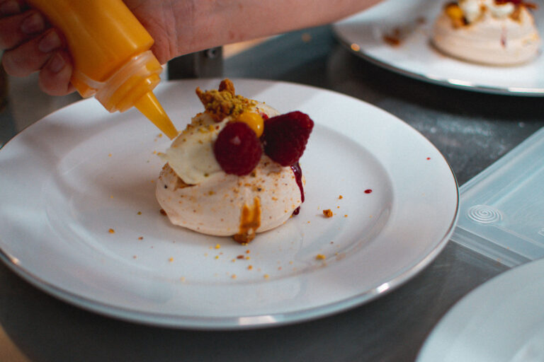 A meringue dessert with raspberries being finished with sauce at the pass, Borthwick Castle