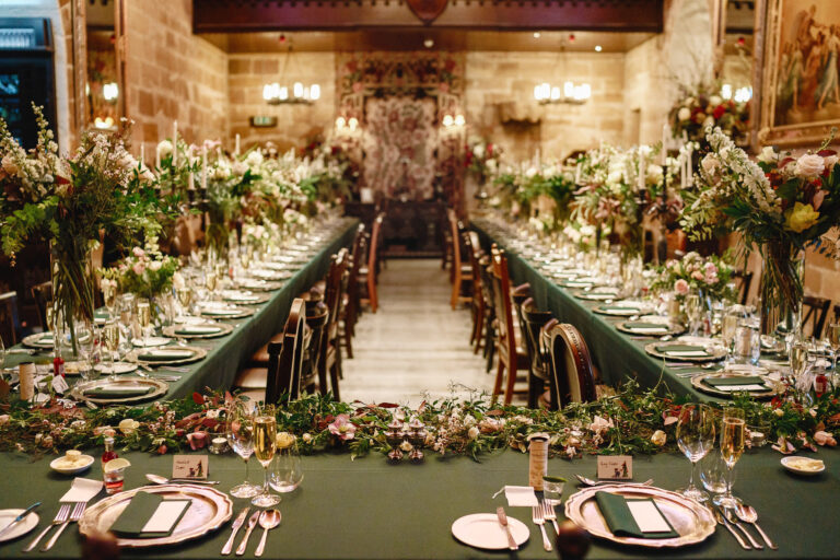 Long tables in the Great Hall dressed with green linen, gold chargers and tall meadow flower arrangements, Borthwick Castle