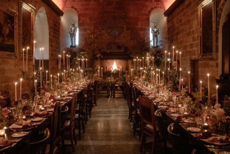 The Great Hall at night with tables lit by dozens of tall candles and the fire burning at the end of the room, Borthwick Castle