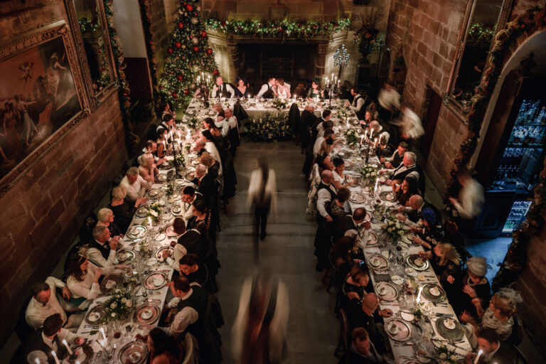 A winter wedding dinner in the Great Hall seen from above, with garlands, candles and staff moving between the long tables, Borthwick Castle