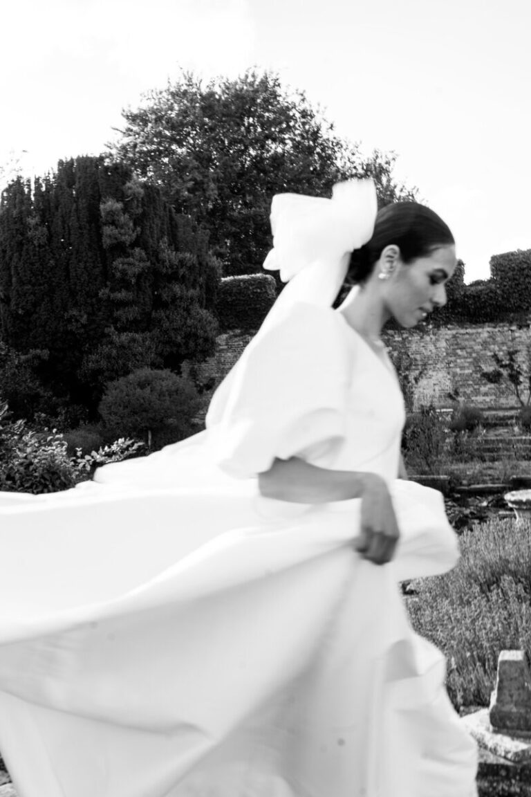 A bride mid-stride through a walled garden, veil caught in the wind, Botias