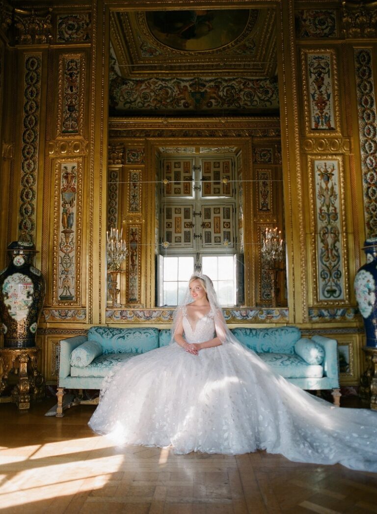 A bride pauses beneath gilt mirrors in a gold-panelled room, her gown pooling around her, Botias