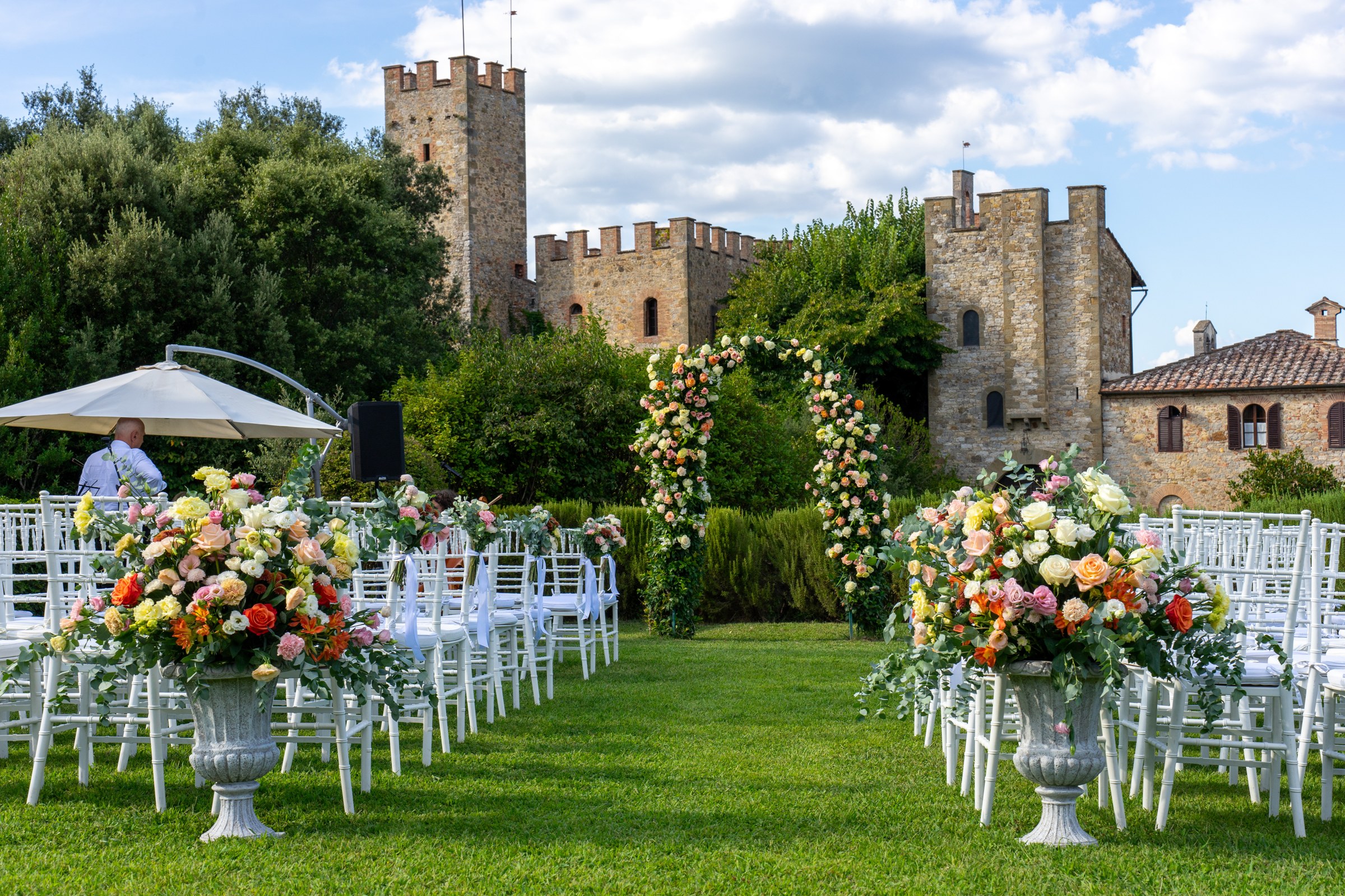 Ceremony lawn at a Tuscan castle, with a floral arch and urns of mixed flowers, Bottega dei Fiori by Ezio De Angelis