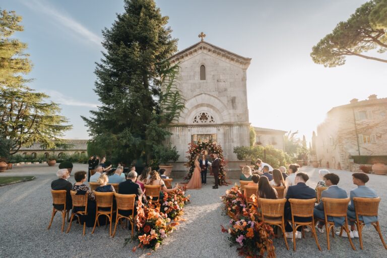 Wedding ceremony in front of a stone chapel, with orange and rust flowers along the aisle, Bottega dei Fiori by Ezio De Angelis