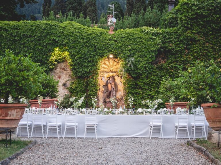 Long banquet table in a hedged garden with white flower arrangements, Bottega dei Fiori by Ezio De Angelis