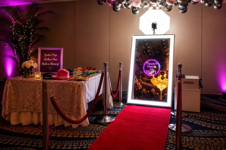 A framed mirror photo booth on a red carpet with a styled prop table, Box Entertainment
