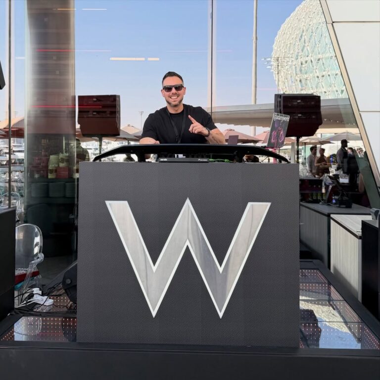 A DJ plays from a branded booth on a hotel terrace by the water, Box Entertainment