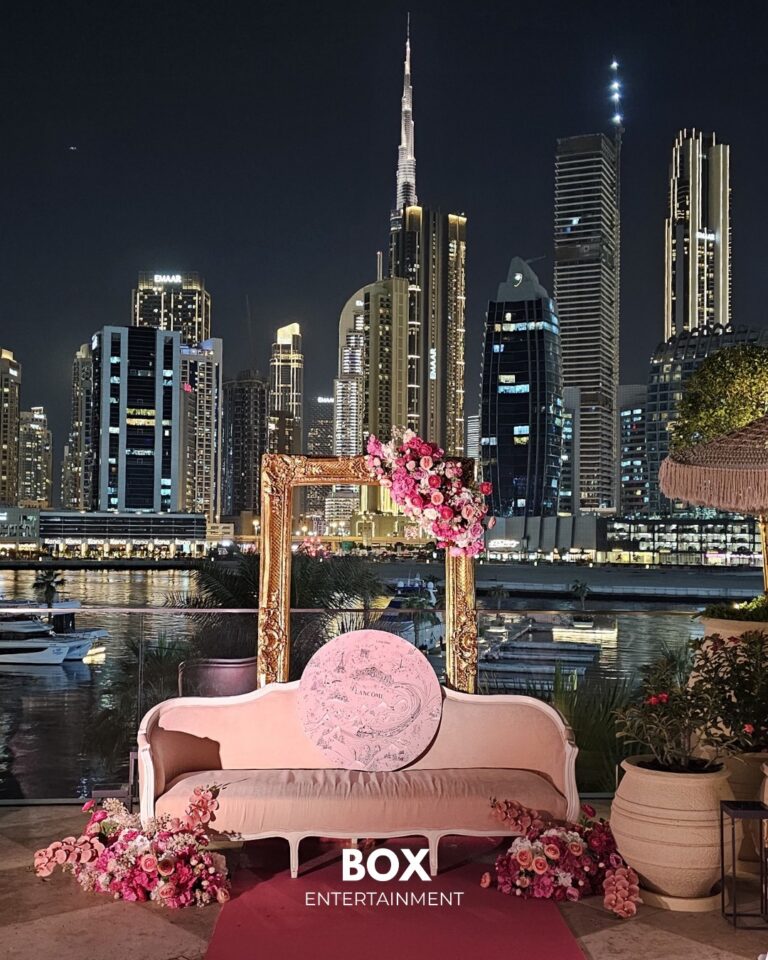 A styled pink sofa and floral frame set against the Dubai skyline at night, marked with the Box Entertainment name, Box Entertainment