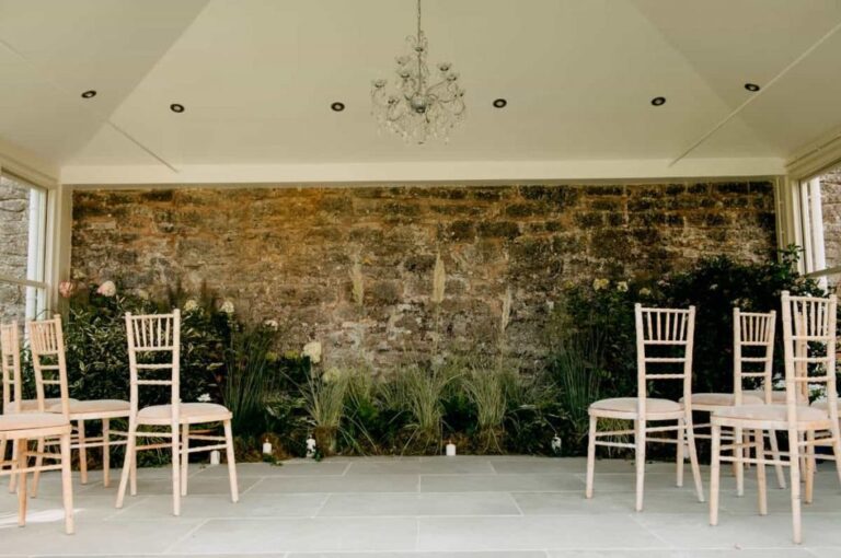 The ceremony room, an exposed stone wall, a chandelier and dressed chairs, Briery Hill House