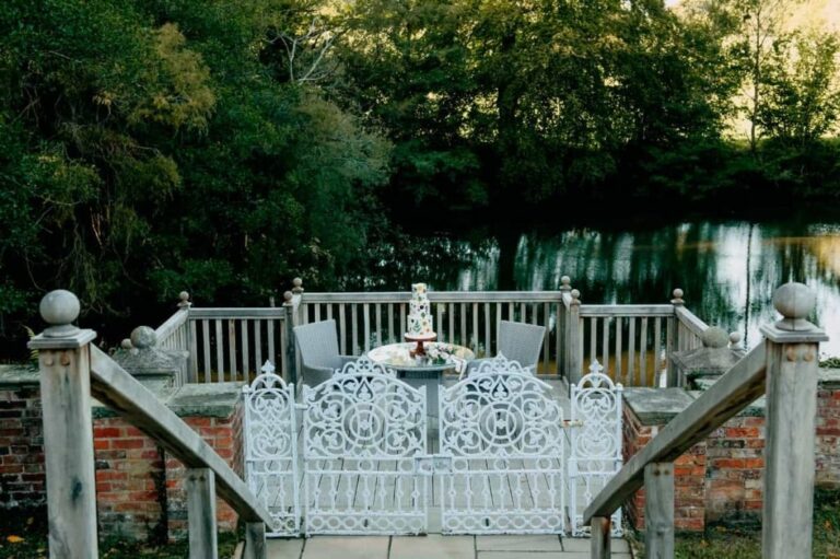 An ornate white cast-iron garden bench set with a cake beside the pond, Briery Hill House